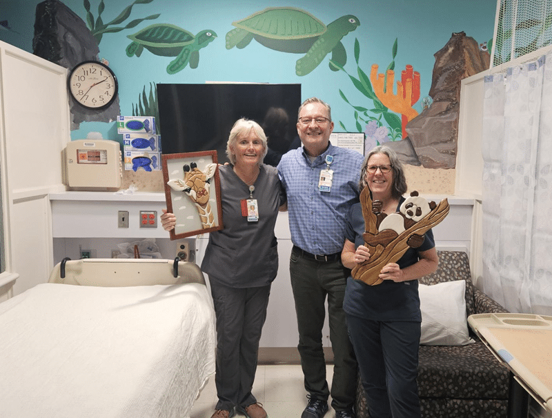 James Robinson stands between two healthcare providers holding his artwork.