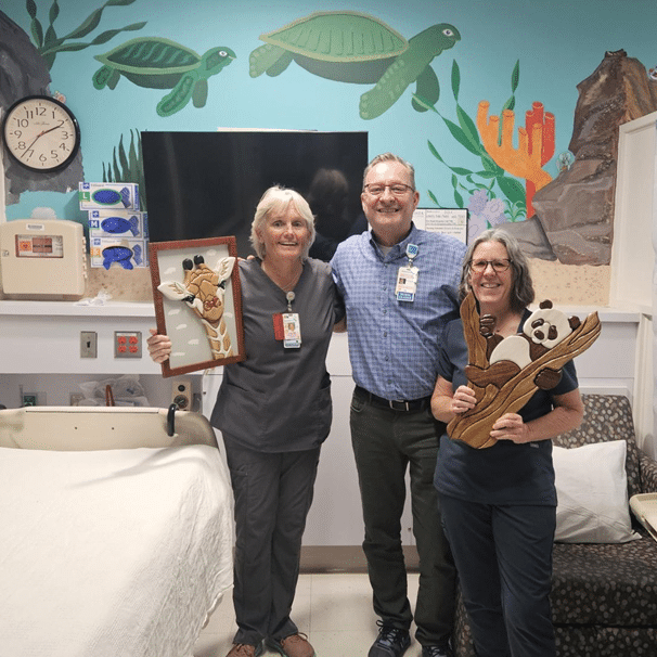 James Robinson stands between two healthcare providers holding his artwork.